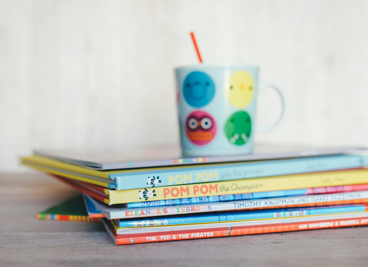 Colorful children's books topped with a mug and straw.