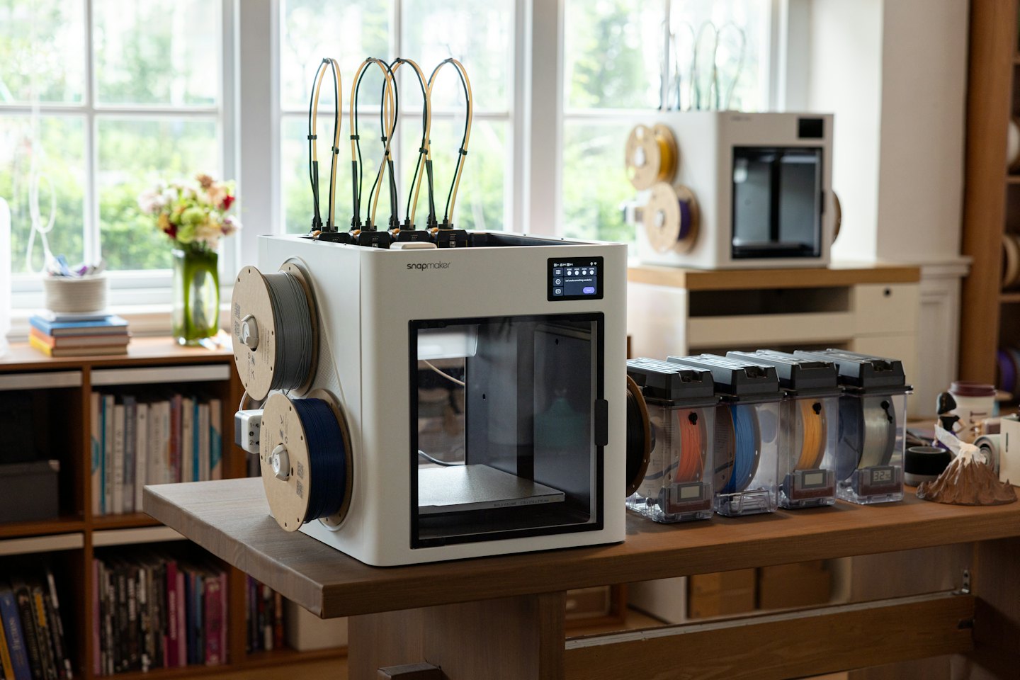A white 3D printer with filament spools on a wooden table.