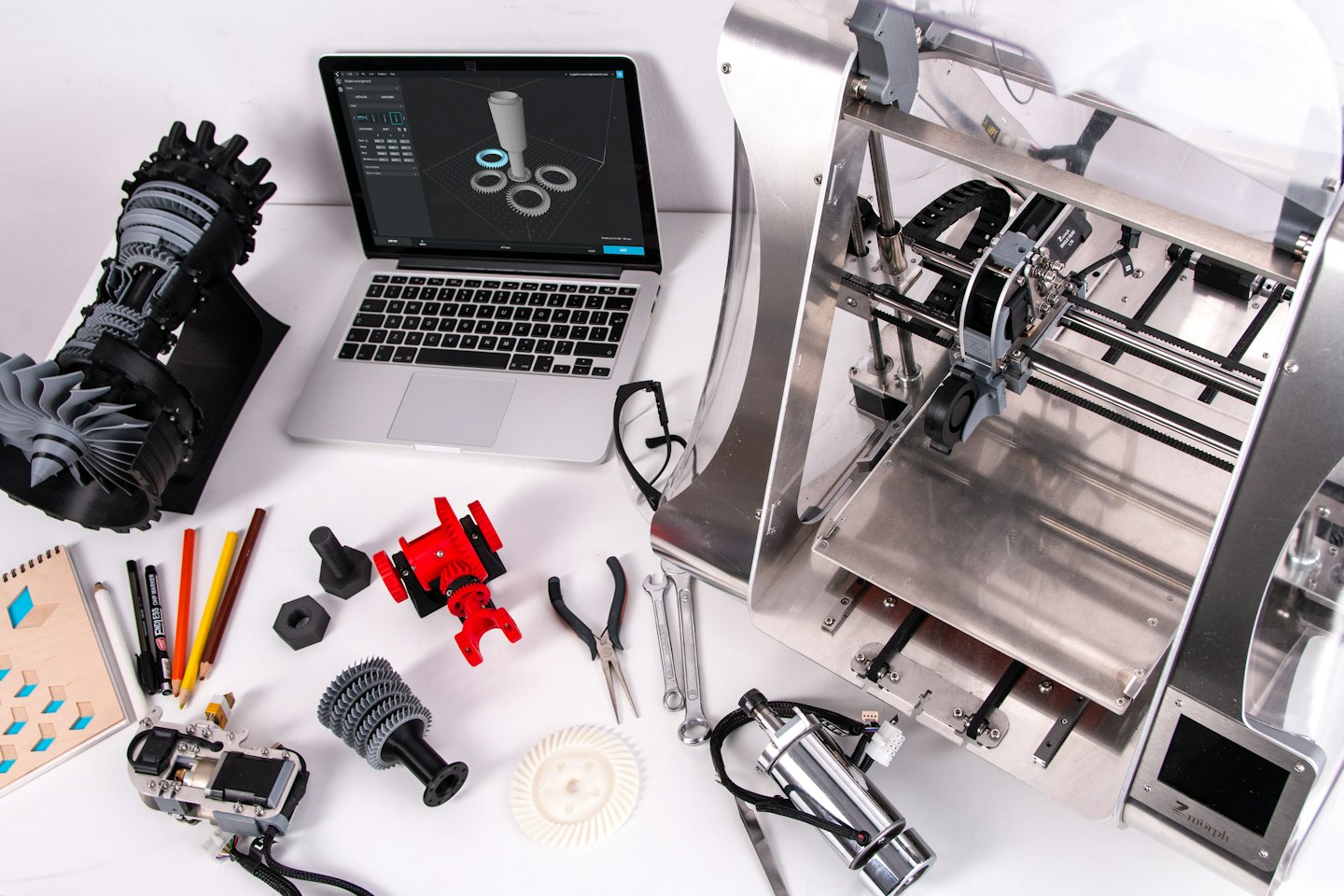 Laptop and 3D printer on a white desk with prototypes.